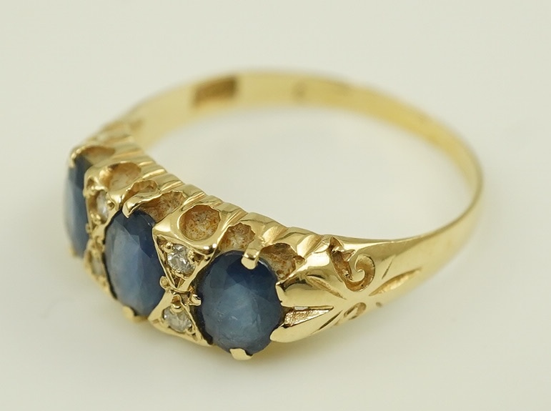 An Edwardian 15ct gold and three stone oval cut sapphire set half hoop ring, with diamond chip spacers, size Q, gross weight 2.4 grams. Condition - poor to fair